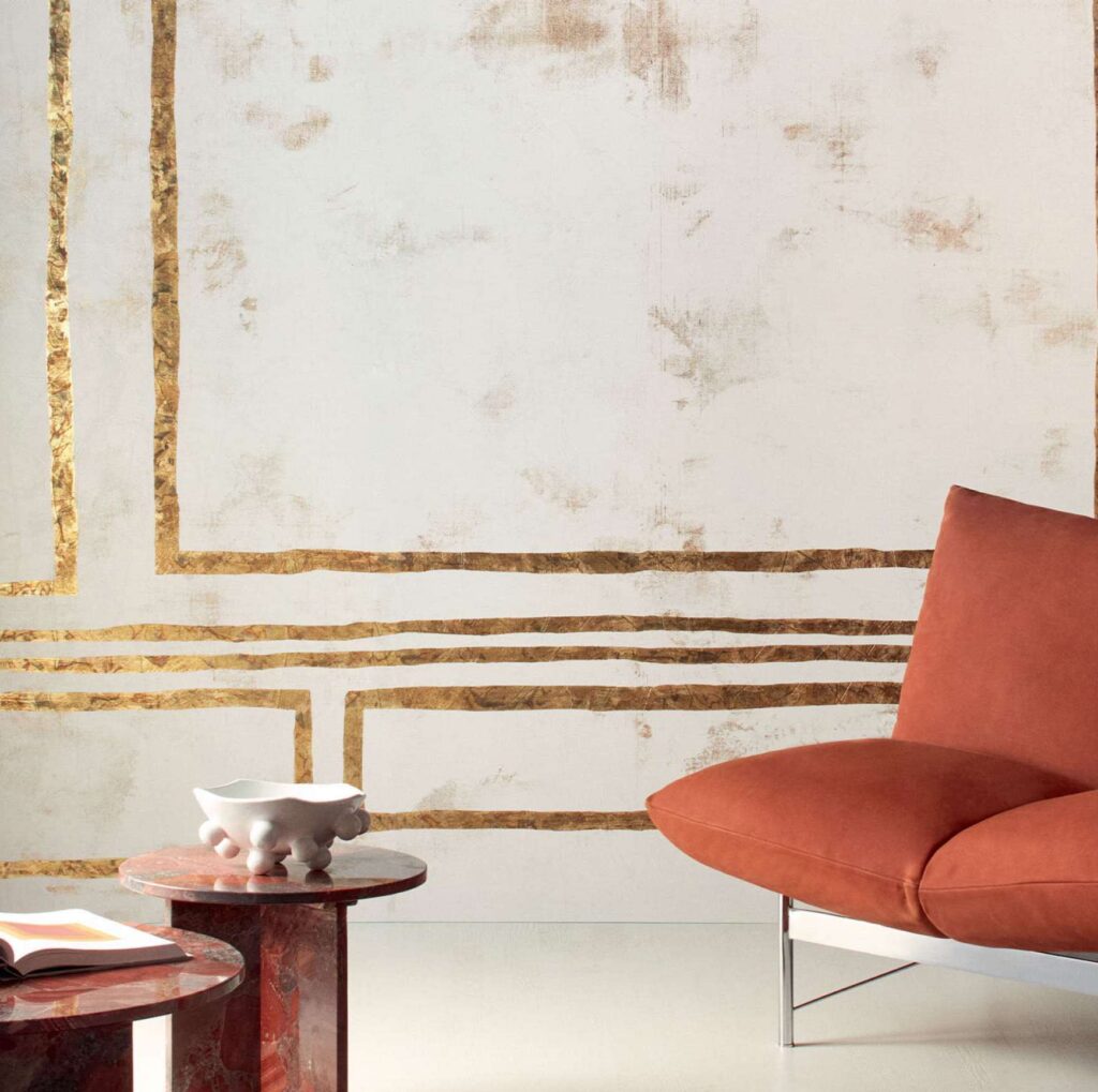 Moderne interieursetting met een Elitis Kintsugi wandbekleding, een roestbruine designstoel en marmeren bijzettafels.