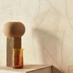Beige Elitis Kintsugi wandbekleding met subtiele reliëfstructuur, gecombineerd met een decoratieve vaas en amberkleurig glasobject op een tafel.