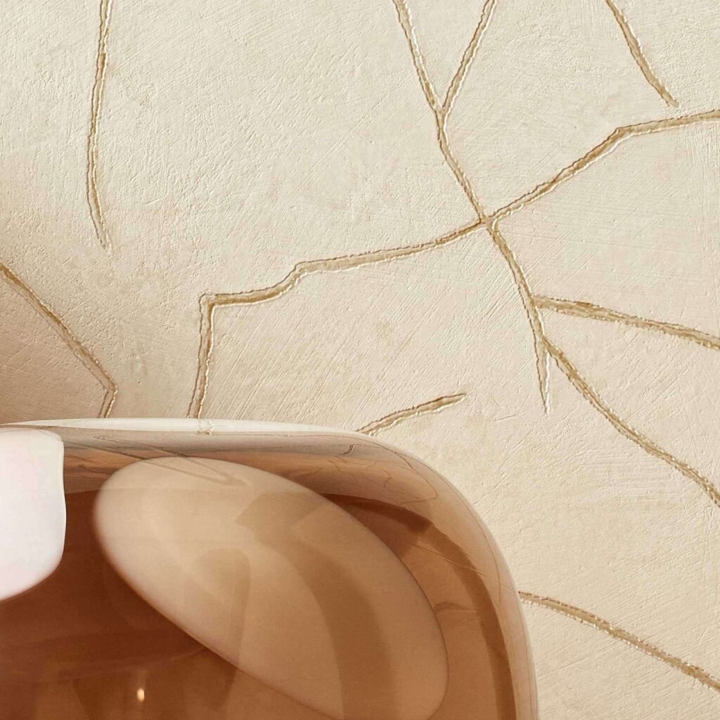 Beige Elitis Kintsugi muur met gouden breuklijnen en een glanzend bruin decoratief object op de voorgrond.
