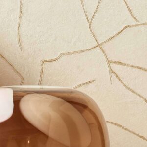 Beige Elitis Kintsugi muur met gouden breuklijnen en een glanzend bruin decoratief object op de voorgrond.