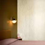 Sfeervolle slaapkamer met Elitis Le Jardin d’Aloès behang in reliëf en een wandlamp op een olijfgroene muur.