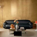 Zwarte designbank voor een goudkleurige Elitis Le Jardin d’Aloès Palimpseste wandbekleding met ronde salontafel en decoratieve objecten.