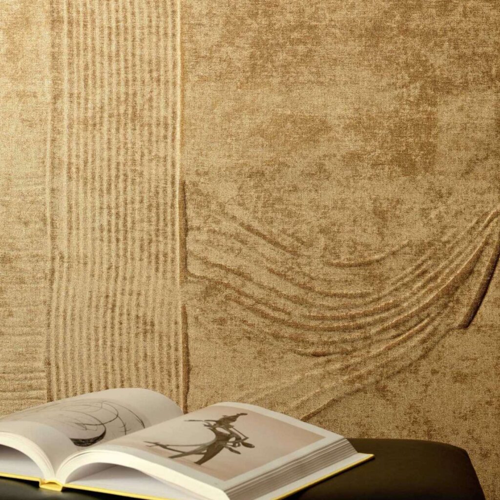 Een openliggend boek ligt op een donkere tafel voor een Elitis Le Jardin d’Aloès Palimpseste RM 1092 04 wandbekleding met reliëfstructuur in warme beige tinten.