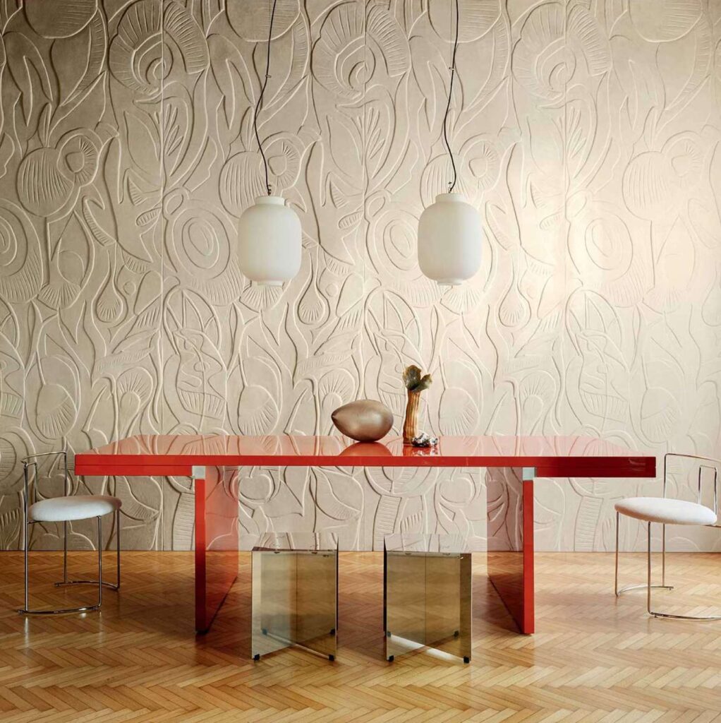 Moderne eetkamer met een roodglanzende tafel en artistiek reliëfbehang uit de Elitis Le Jardin d’Aloès Colosse Fruitier collectie.