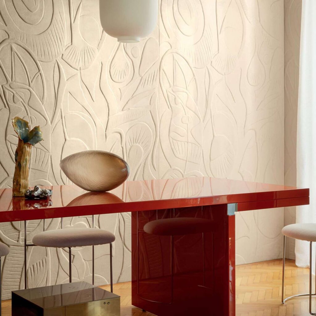 Moderne interieursetting met een glanzende rode tafel, designobjecten en Elitis Jardin d’Aloès Colosse Fruitier reliëfbehang op de achtergrond.