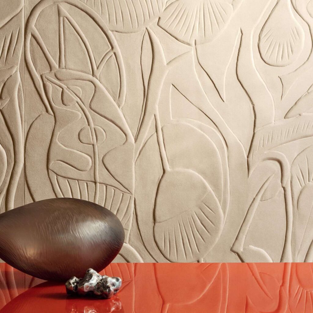 Beige wandbekleding Elitis Le Jardin d’Aloès met abstracte, reliëfachtige plantenmotieven en decoratieve objecten op een rode ondergrond.