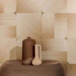 Twee aardewerken vazen staan op een ronde tafel voor een decoratieve Elitis Maestria Circe RM 1072-01 wandbekleding met geometrisch patroon in beige tinten.