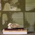 Decoratieve opstelling met boeken en een sculptuur voor een Elitis Maestria Kalliste RM 1077 02 wandbekleding met groen geometrisch reliëfpatroon.