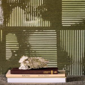 Decoratieve opstelling met boeken en een sculptuur voor een Elitis Maestria Kalliste RM 1077 02 wandbekleding met groen geometrisch reliëfpatroon.