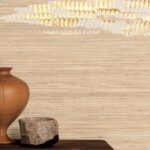 Detail van Elitis Maestria Orion RM 1075 80 crèmekleurig behang met goudaccenten, met een houten vaas en keramisch potje op een houten oppervlak.