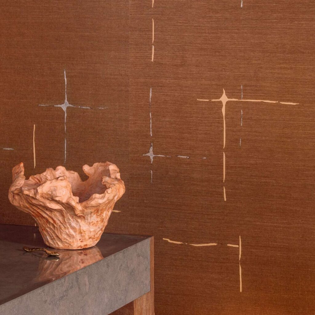Zittende voor een muur bekleed met Elitis Maestria Orphée RM 1076-55 behang staat een decoratieve, aardekleurige schaal op een stenen bijzettafel.
