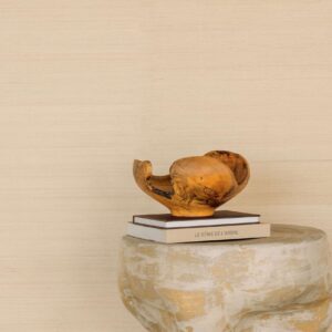 Houten sculptuur op boeken en betonnen tafel tegen een beige Elitis Maestria Pur Abaca RM 1071-01 wandbekleding.