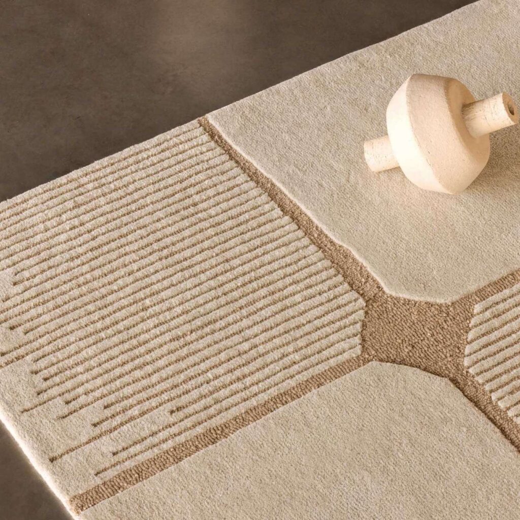 Detail van het Elitis Marcel TA 134 03 06 vloerkleed met een geometrisch reliëfpatroon in beige en crème.