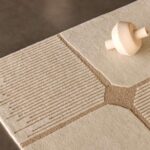 Detail van het Elitis Marcel TA 134 03 06 vloerkleed met een geometrisch reliëfpatroon in beige en crème.