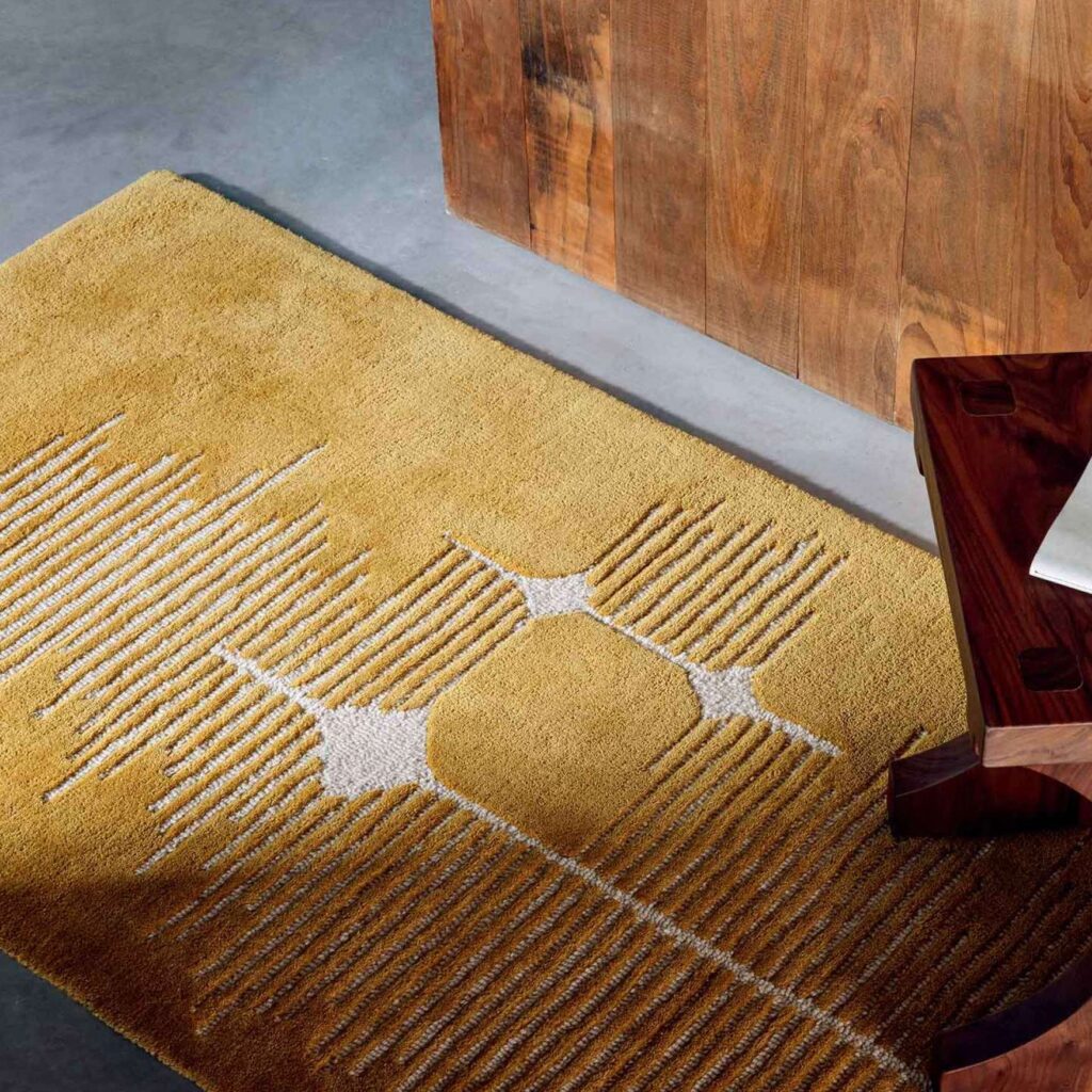 Geel Elitis Marcel TA 134 25 06 vloerkleed met geometrisch patroon in een moderne interieursetting.