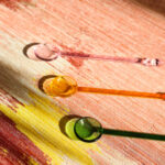 Drie gekleurde glazen lepels liggen op een abstract bloemrijk Elitis-behang in warme tinten.