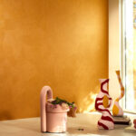 Moderne interieursetting met een okergele Elitis Circolo VP 976 wandbekleding, organisch gevormde vazen en een roze designstoel.