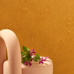 Roze designstoel met bloemen tegen een oranje Elitis Circolo-structuurbehang met grafisch patroon.