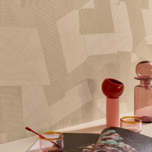 Sfeervolle interieursetting met Elitis Dédales VP 975 03 behang met geometrisch patroon op de achtergrond en decoratieve roze glazen objecten op de voorgrond.