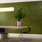 Modern interieur met Elitis Matières à Réflexions Dédales VP 975 60 behang in groen, met designmeubels en een vaas met bloemen op een tafel.
