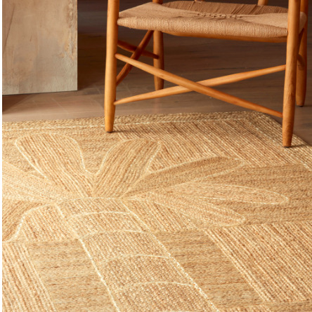 Detailopname van het Elitis Mirador indoor vloerkleed TA 127 05 05 met een palmbladmotief, naast een houten stoel.
