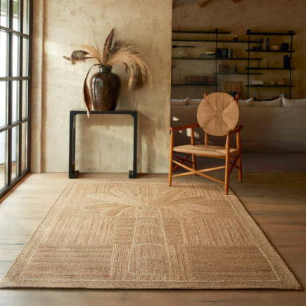 Natuurlijke en warme woonkamer met het Elitis Mirador TA 127 05 05 vloerkleed, een houten stoel en een vaas met droogbloemen.