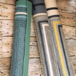 Drie opgerolde Elitis outdoor vloerkleden uit de Disco TA 113-26-05 collectie liggen tegen een houten wand.