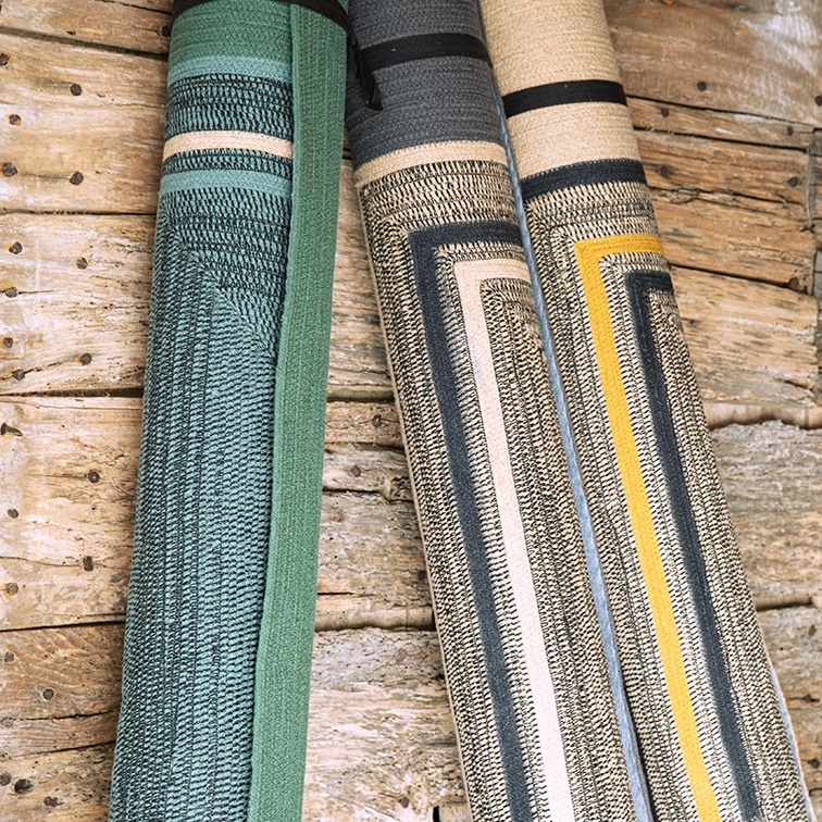 Drie opgerolde Elitis outdoor vloerkleden uit de Disco TA 113-26-05 collectie liggen tegen een houten wand.