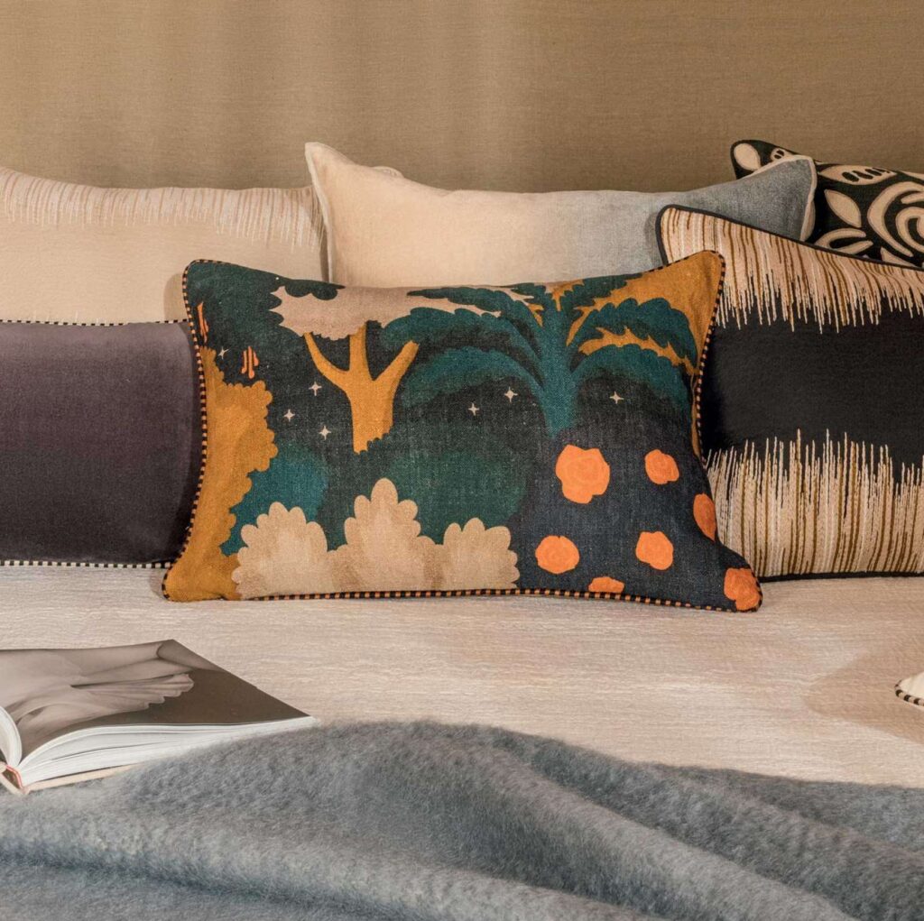 Decoratief Elitis Paul CO 258 34 02 kussen met kleurrijk boom- en bloemenpatroon op een opgemaakt bed met meerdere sierkussens.