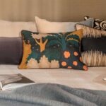 Decoratief Elitis Paul CO 258 34 02 kussen met kleurrijk boom- en bloemenpatroon op een opgemaakt bed met meerdere sierkussens.