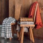 Twee houten stoelen met daarop en eroverheen gedrapeerde Elitis plaids in verschillende kleuren en ruitpatronen.