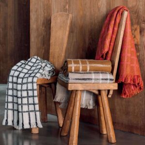 Twee houten stoelen met daarop en eroverheen gedrapeerde Elitis plaids in verschillende kleuren en ruitpatronen.