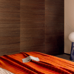 Een slaapkamer met een Elitis plaid Edith PL 307 36 in warme oranjetinten over het bed en een open boek erop.