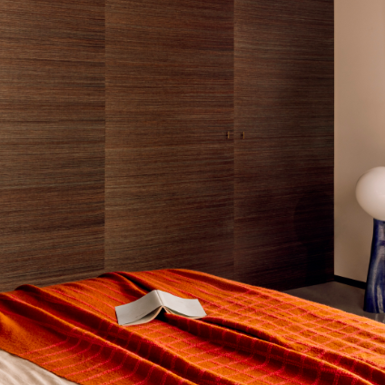 Een slaapkamer met een Elitis plaid Edith PL 307 36 in warme oranjetinten over het bed en een open boek erop.