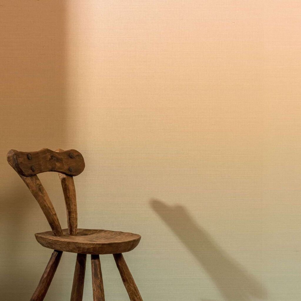 Houten stoel voor een wand met Elitis Poesies de l’Instant RM 1082 02 behang in warme beige tint.