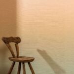 Houten stoel voor een wand met Elitis Poesies de l’Instant RM 1082 02 behang in warme beige tint.