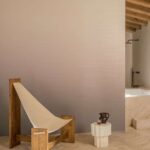 Minimalistisch interieur met Elitis Poesies de l’Instant RM 1082 04 behang, een houten loungestoel en een natuurstenen bijzettafel.