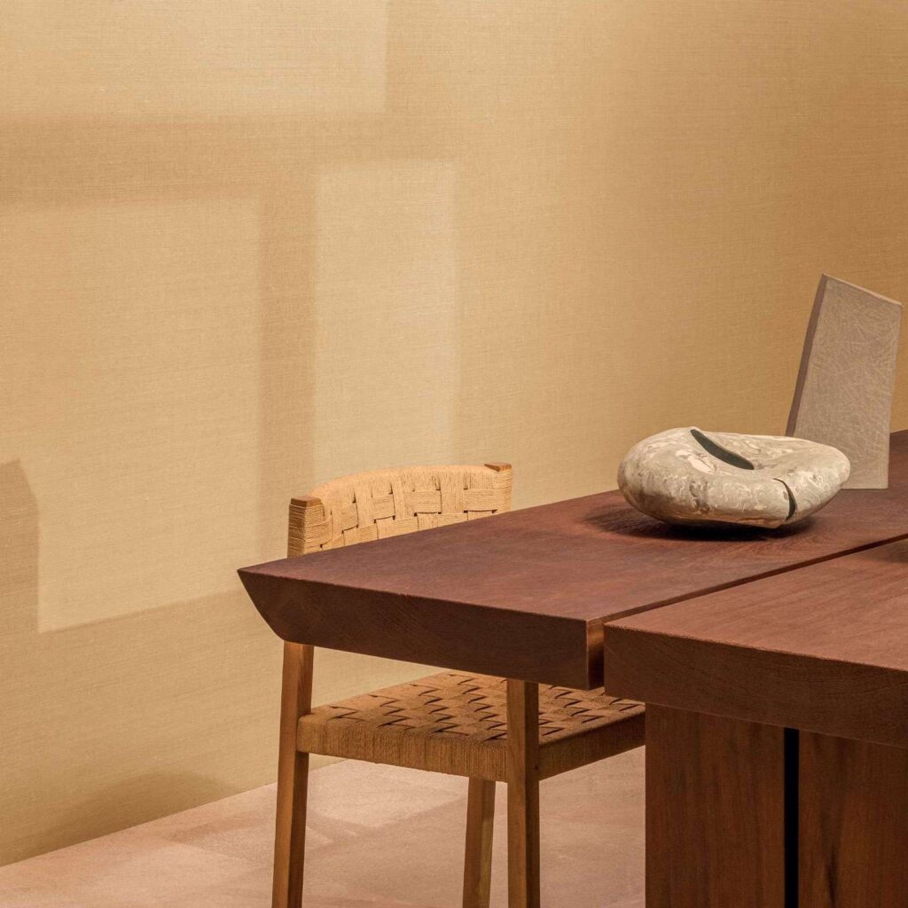 Stijlvolle interieuropsetting met Elitis Poesies de l’Instant RM 1082 08 behang, houten tafel en geweven stoel.