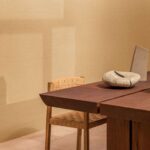 Stijlvolle interieuropsetting met Elitis Poesies de l’Instant RM 1082 08 behang, houten tafel en geweven stoel.