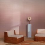 Twee houten loungestoelen en een beeld op sokkel staan in een interieur met Elitis Poesies de l’Instant RM 1082 13 behang in zachte roze tinten.