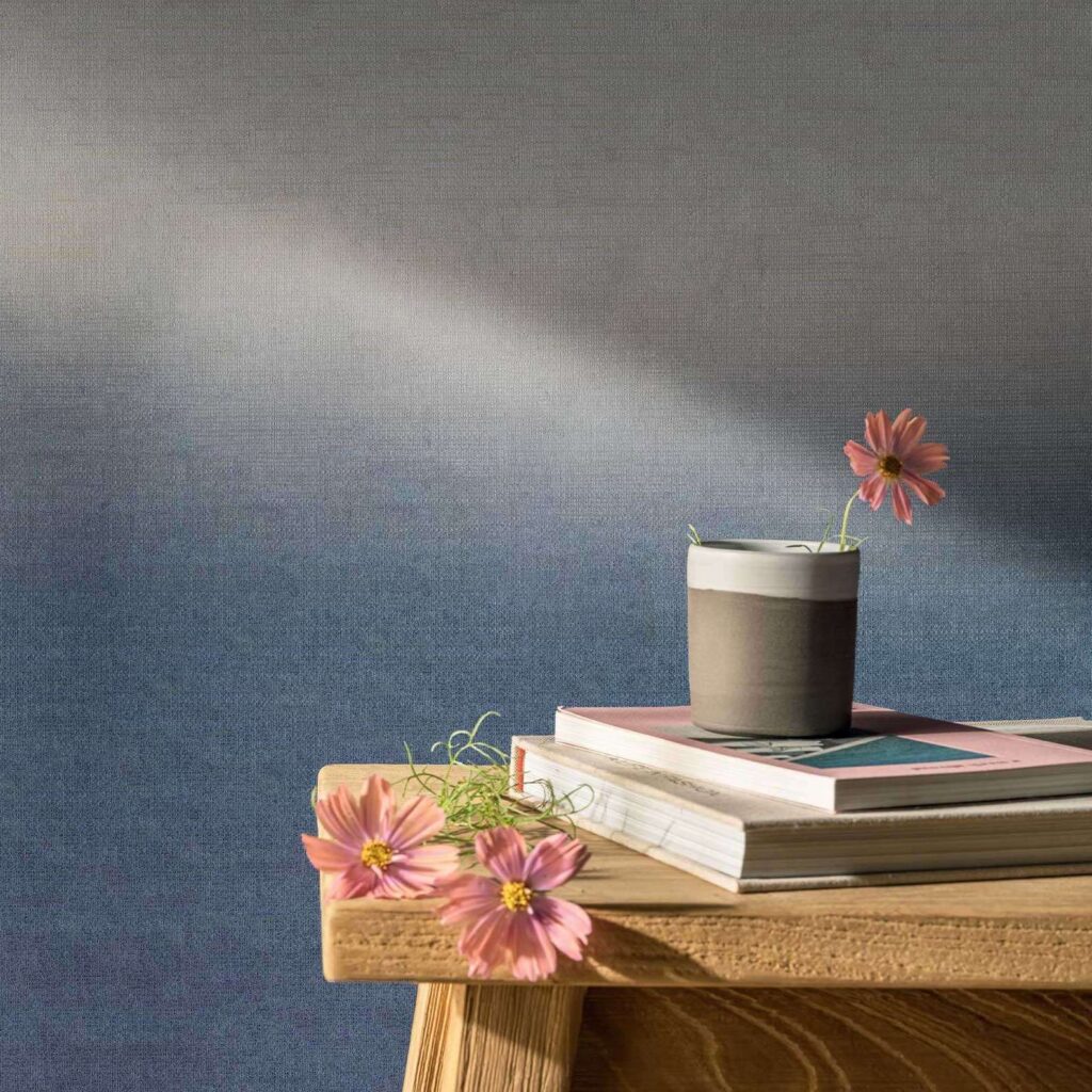 Houten tafel met bloemen, boeken en een kopje tegen een blauw Elitis Poesies de l’Instant RM 1082 16 behang.
