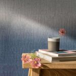 Houten tafel met bloemen, boeken en een kopje tegen een blauw Elitis Poesies de l’Instant RM 1082 16 behang.