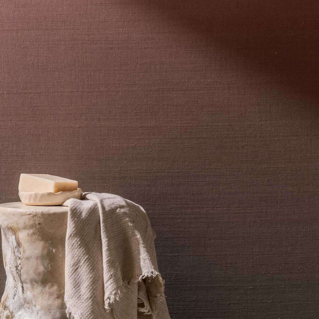 Sfeervolle interieurfoto met Elitis Poesies de l’Instant RM 1082 20 behang, een stoffen doek, en een stuk zeep op een keramische kruk.