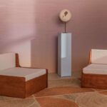 Twee houten loungefauteuils met licht beklede kussens staan tegenover elkaar in een minimalistisch interieur met Elitis Rocky wandbekleding en sculptuur op sokkel.