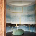 Moderne zithoek met Elitis Sangpi Brumes Laquées behang, een ronde groene poef en een klein wit tafeltje met decoraties.