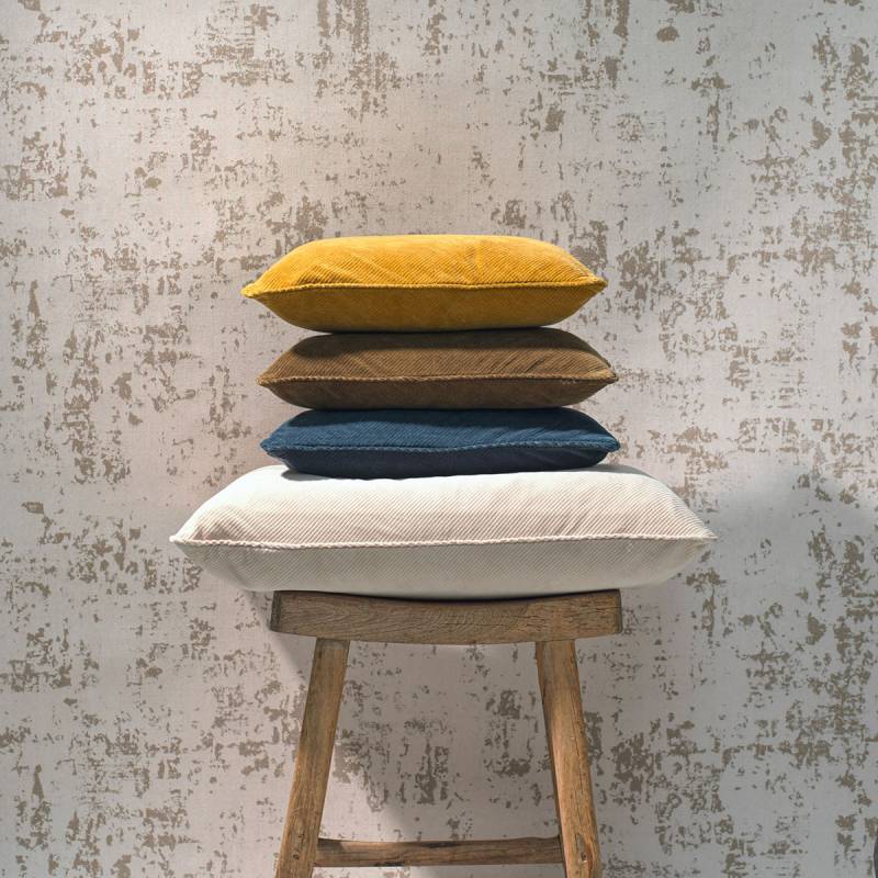 Vier Elitis sierkussens uit de Itaque-serie in verschillende kleuren, gestapeld op een houten kruk tegen een decoratieve muur.