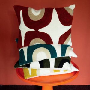 Stapel sierkussens uit de Elitis Nirvana collectie met kleurrijke, grafische patronen op een oranje bijzettafel.