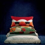 Stapeling van drie Elitis sierkussens, met bovenop het Celestine CO 252 37 7 kussen met rood, zwart en wit patroon.