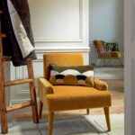 Mosterdgele fauteuil met het Elitis sierkussen Celestine CO-252 in een sfeervol ingericht interieur.