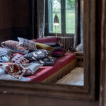 Sierkussens uit de Elitis Motu-collectie liggen op een bed in een sfeervol ingericht vertrek met uitzicht op een tuin.
